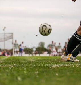 Homem chutando uma bola de futebol em direção ao gol