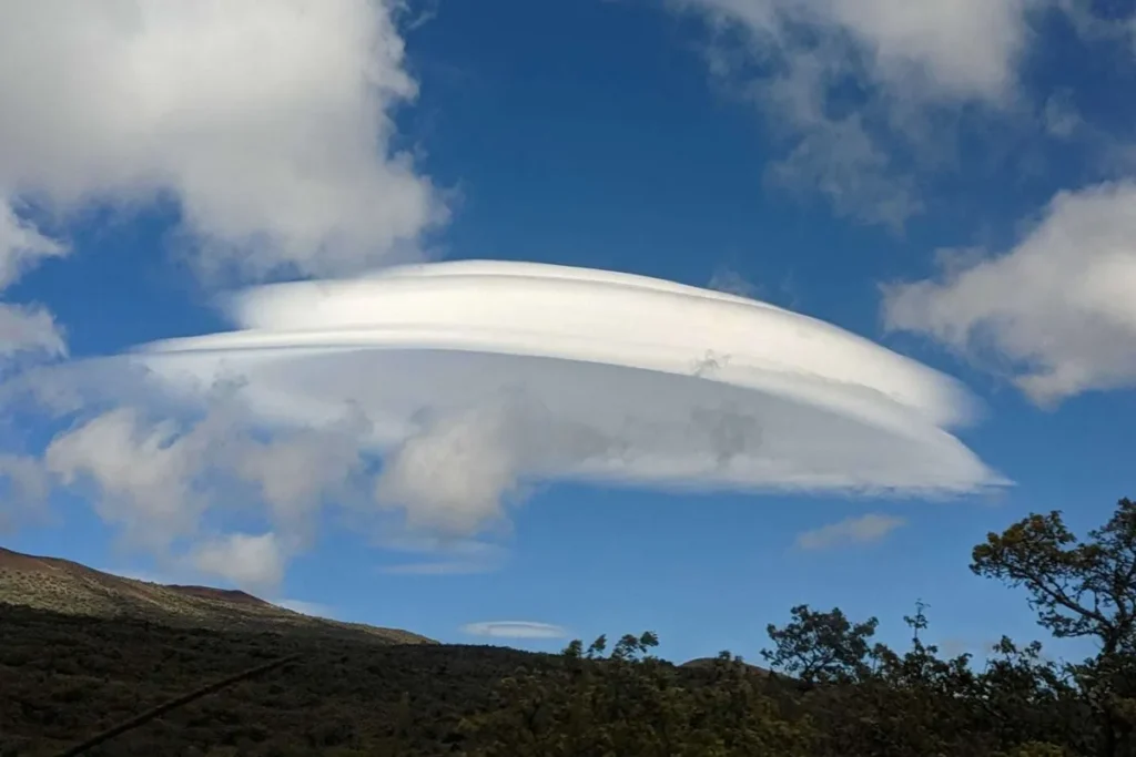 Nuvem lenticular branca em formato de disco sobre montanhas, destacando-se no céu azul com nuvens dispersas.