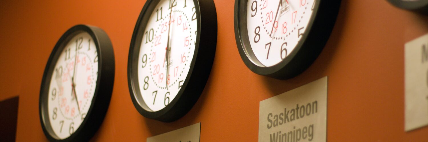 Parede laranja com vários relógios mostrando diferentes fusos horários.