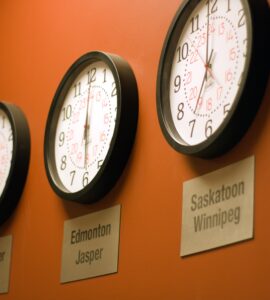 Parede laranja com vários relógios mostrando diferentes fusos horários.