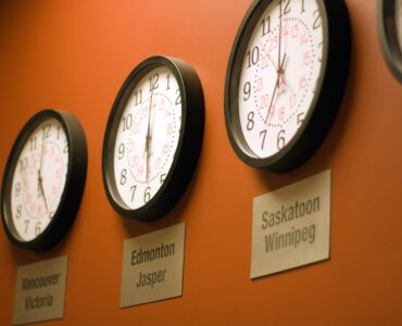 Parede laranja com vários relógios mostrando diferentes fusos horários.