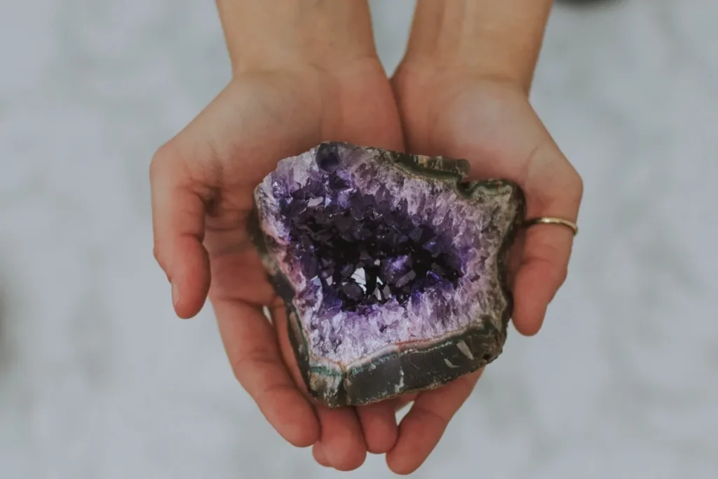 Pessoa segurando um cristal de ametista roxa com forma irregular e interior repleto de pontas brilhantes
