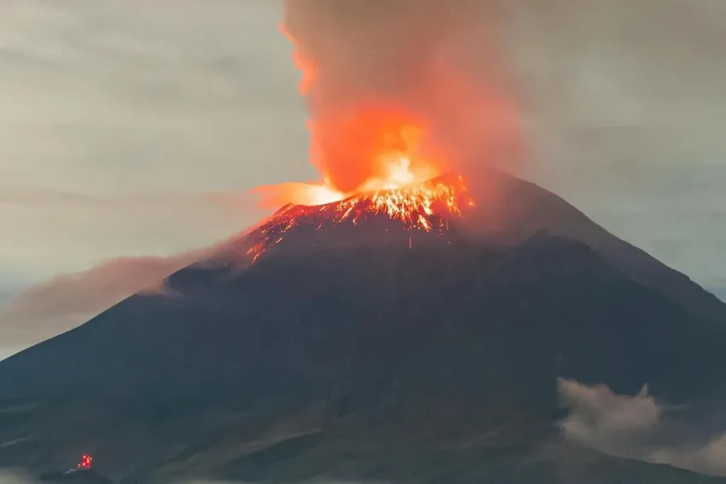 Erupção de um vulcão com lava incandescente e nuvem de fumaça iluminando o céu noturno