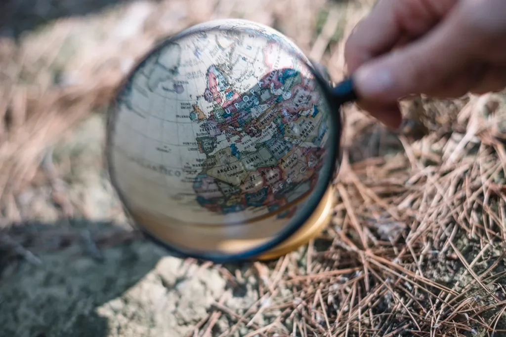 Mão segura lupa sobre globo terrestre ampliando a região da Europa e norte da África, representando estudo geográfico