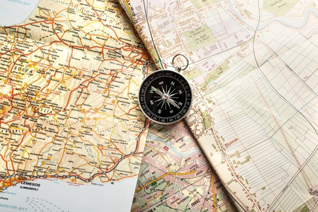 Bússola posicionada sobre mapas rodoviários e topográficos detalhados, destacando cidades, estradas e áreas rurais.