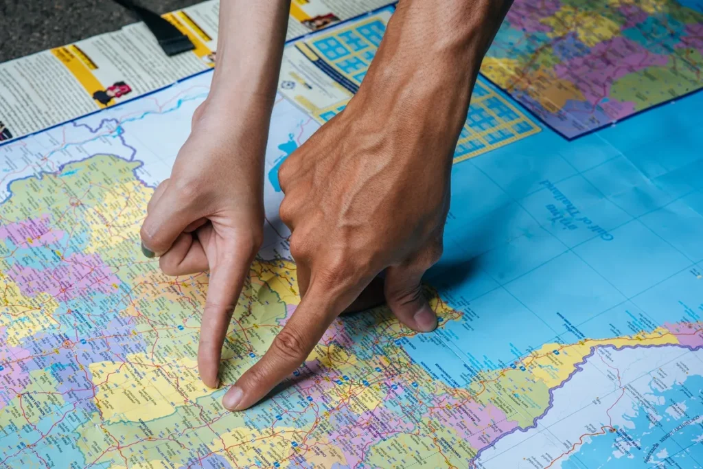 Duas mãos apontando diferentes locais em um mapa político colorido, indicando rotas e destinos de viagem.