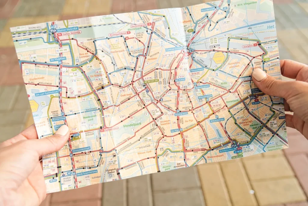 Pessoa segurando um mapa turístico de Amsterdã com destaque para ruas, canais, pontos turísticos e rotas de transporte público.