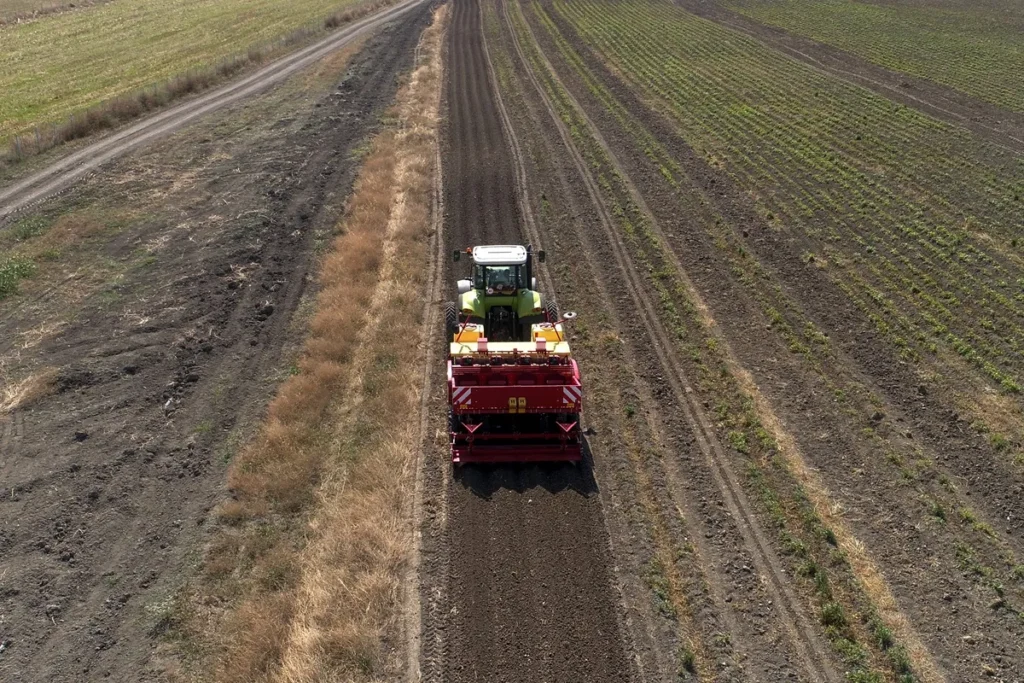 Trator com implemento agrícola vermelho realiza compactação e preparo do solo em lavoura, formando linhas de cultivo organizadas.