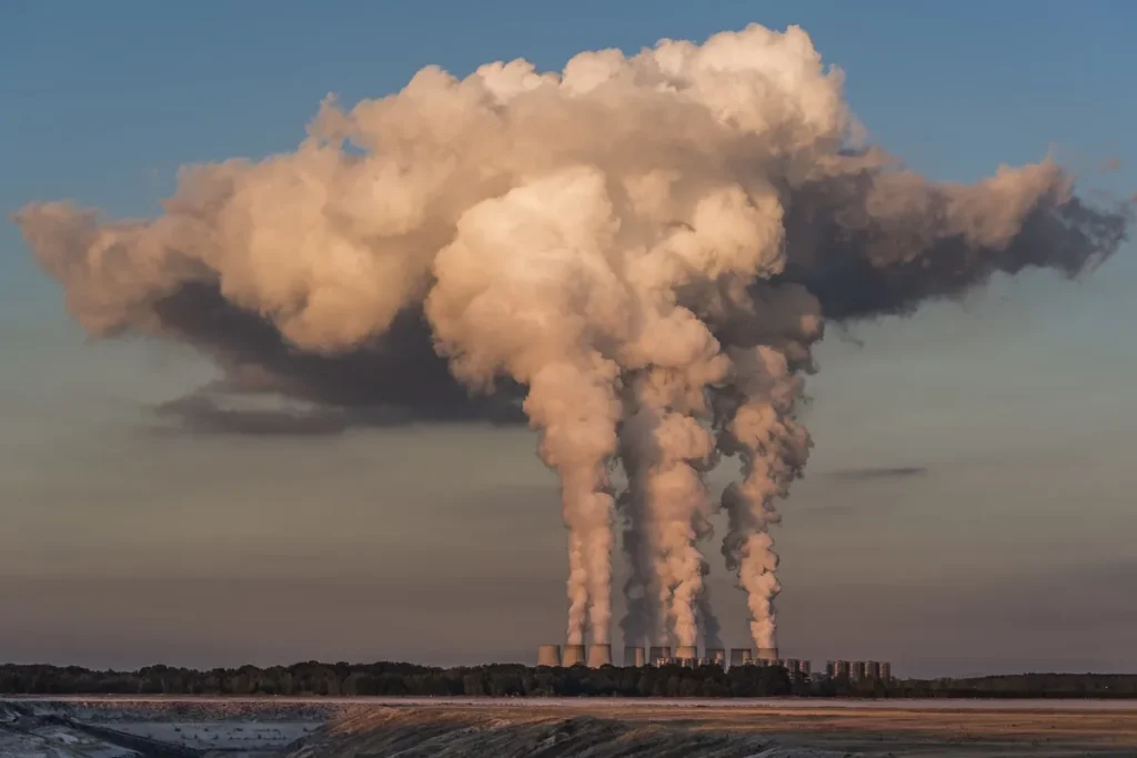 Grandes colunas de fumaça saindo de chaminés industriais, representando poluição atmosférica e emissão de gases de efeito estufa