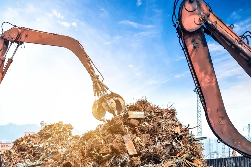 Escavadeiras industriais movimentando pilha de sucata metálica para reciclagem sob céu azul.