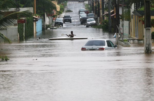 Foto de enchente no município de Lauro de Freitas, com carros submersos e uma pessoa andando de caiaque no meio da rua.