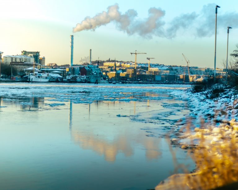 Imagem de rio poluído à beira de uma fábrica soltando fumaça.