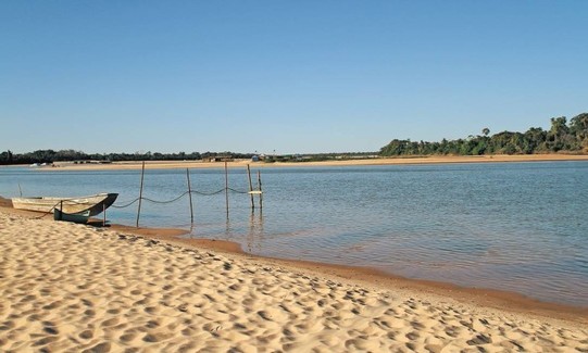 Imagem de uma planície, uma praia com areia e vegetação ao fundo.
