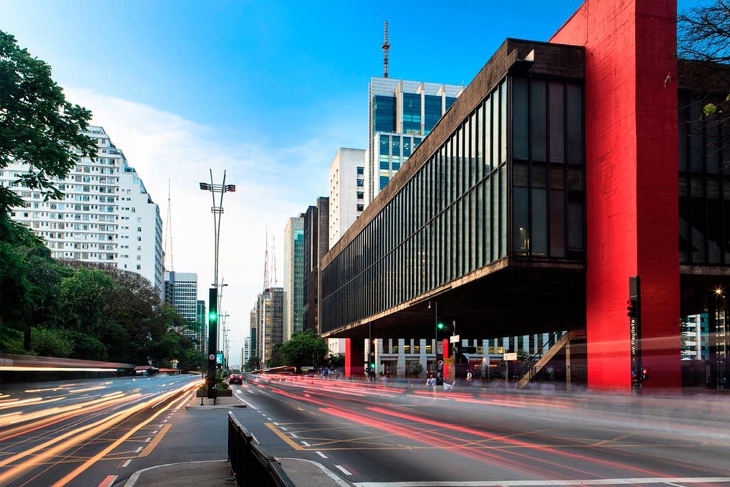 Foto do Museu de Arte de São Paulo, na Avenida Paulista, sem carros na rua. Embaixo do asfalto da avenida, encontram-se argilas vermelhas como perfil de solo.