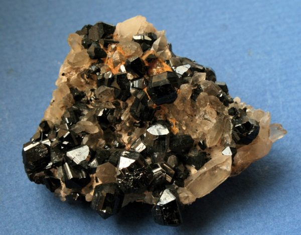 Foto de cristais de cassiterita, mineral muito valioso para a Geologia Econômica, apoiado numa superfície azul.