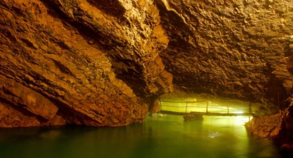 Foto de um lago dentro de uma caverna. Ligando duas pontas da caverna há uma escada de madeira.