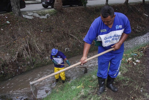 Dois profissionais de uniforme escrito "Guardião dos Rios" fazendo a limpeza de rios com uma pá.
