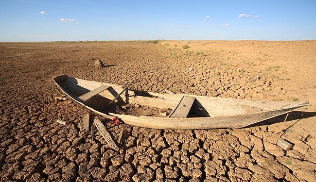 Foto de paisagem de seca no nordeste, com solo ressecado, muito sol e um barco de madeira quebrado em foco. É um exemplo de desastre climatológico.