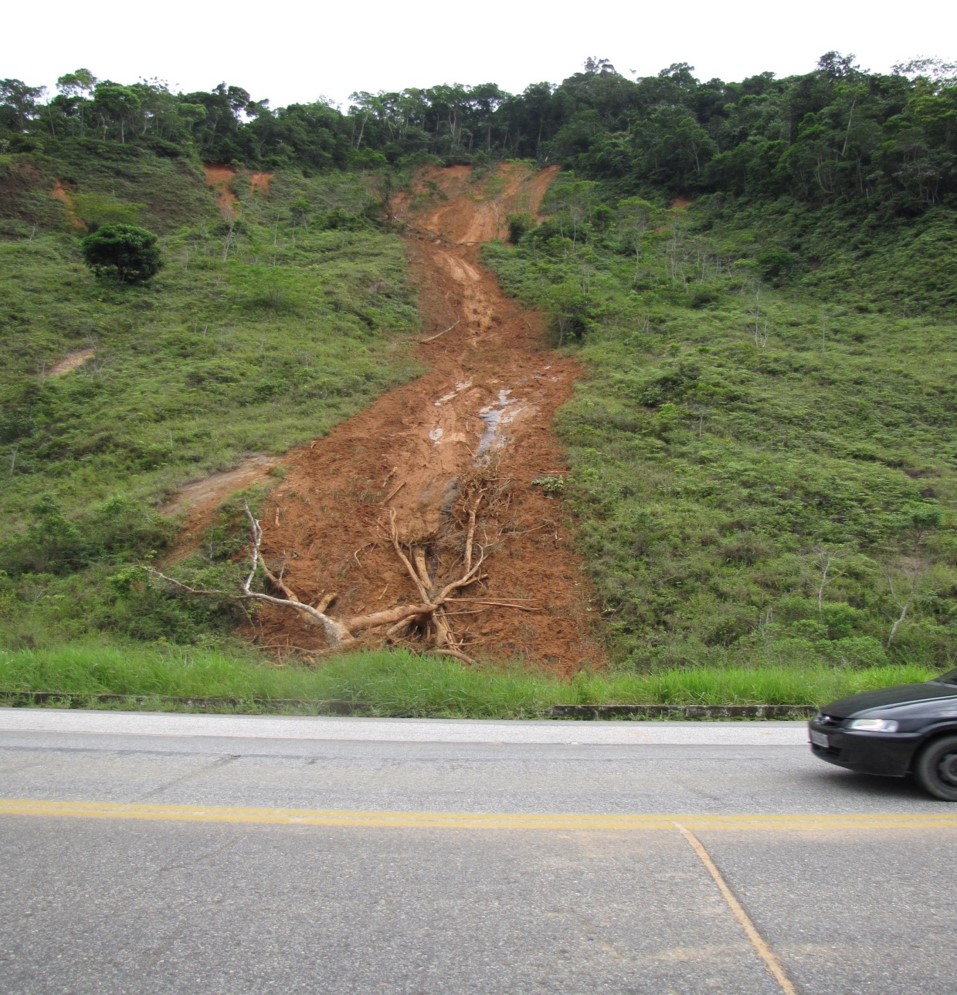 Foto de um deslizamento vertical num morro da estrada Rio-Santos, sem diagnóstico. À direita, um carro passando.