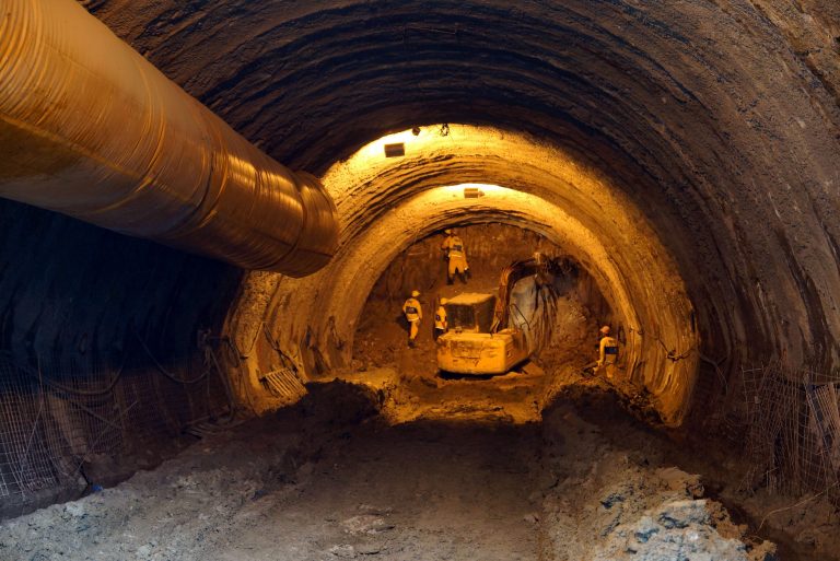 Estabilização de escavações: a foto mostra a escavação de um túnel subterrâneo para alongamento do rio Joana até a Baía de Guanabara, com trabalhadores e máquinas ao fundo.