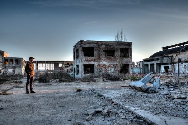 Foto de área atingida pelo acidente nuclear de Chernobyl, na Ucrânia, onde houve irradiação e contaminação. Na foto, um homem está de pé parado em um terreno vazio, com destroços pelo chão e um prédio depredado ao fundo.