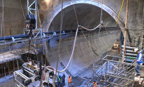 Imagem da construção de um túnel, um dos tipos de obras subterrâneas. Na foto, andaimes, caminhões e operários estão trabalhando na parte elétrica da obra, com cabos sendo posicionados.