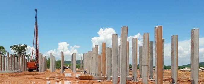 Foto de uma construção, com pilares de concreto se erguendo do solo e uma máquina de perfuração à esquerda.