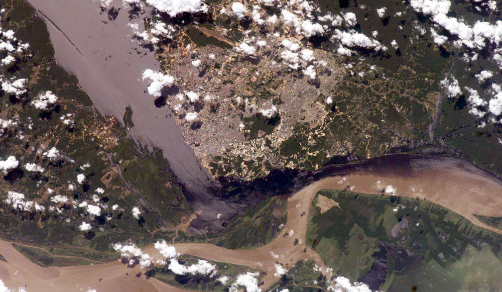 Imagem aérea de uma área com vegetação, cadeias montanhosas e um rio.
