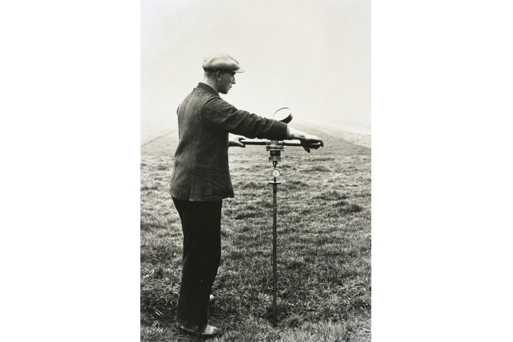 Foto sépia de um homem de uniforme realizando ensaios cpt e cptu num solo com um instrumento de medição. 