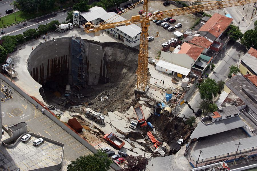 Foto aérea da cratera formada no acidente nas obras da Estação Pinheiros de metrô em 2007, com um andaime amarelo na beirada, quase escorregando para dentro.