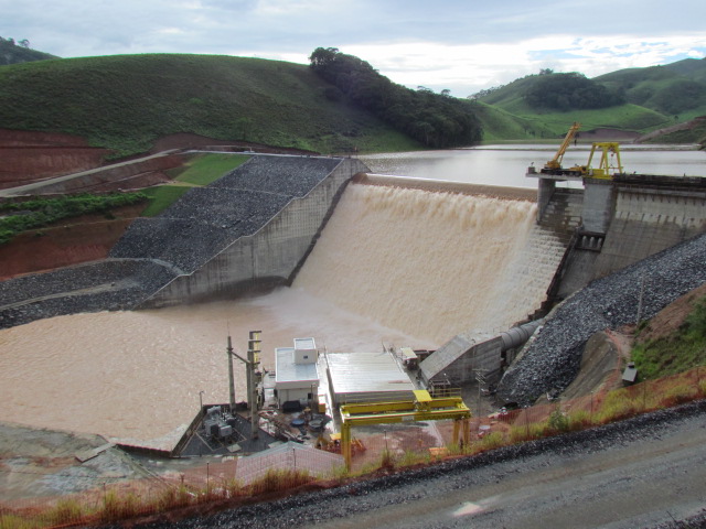 Foto de uma PCH em funcionamento, com água barrenta jorrando da hidrelétrica.