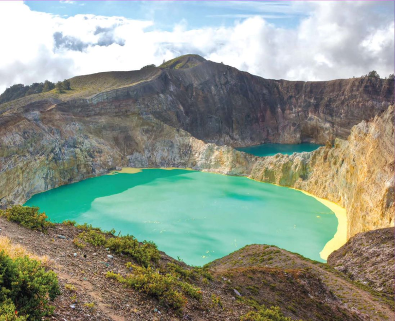 Foto de um depósito mineral, um lago azul em meio a uma cadeia de montanhas, que servem como barreiras geoquímicas.