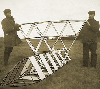 Foto sépia de dois homens segurando uma pipa tetraédrica.