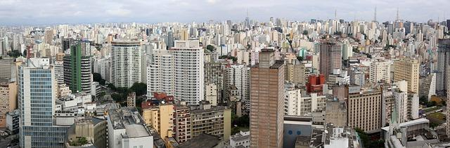 Foto aérea de centenas de prédios em uma cidade, com o horizonte atrás.