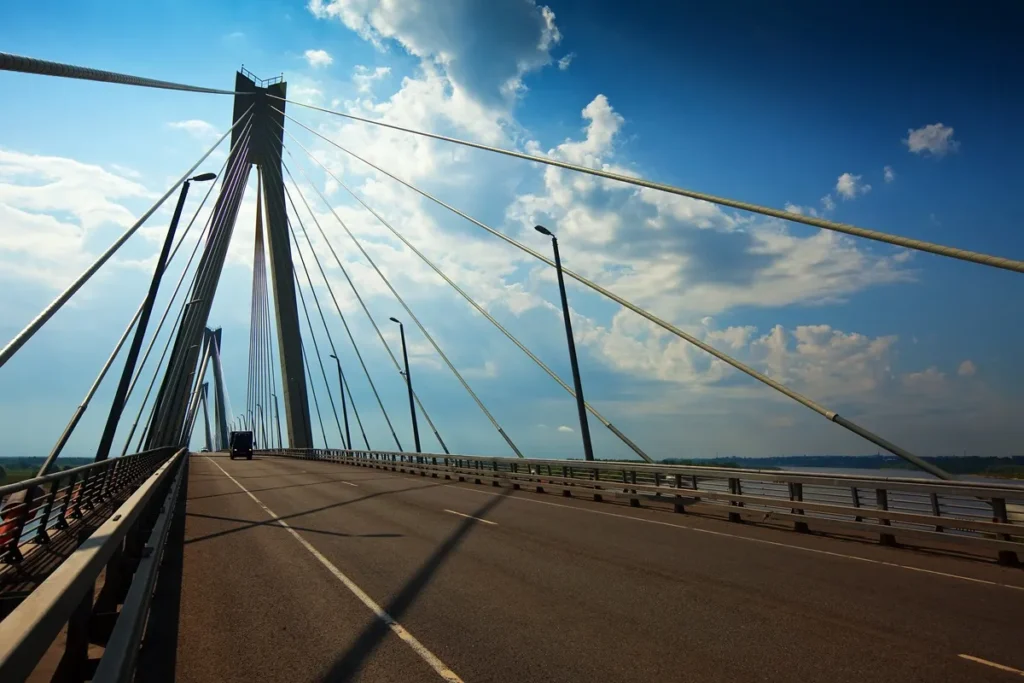 Ponte estaiada com cabos simétricos e pilares altos, sob um céu azul com nuvens iluminadas pelo sol.