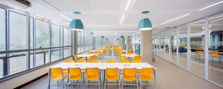Foto de uma sala de aula ampla, com janelas grandes e muita luz entrando.