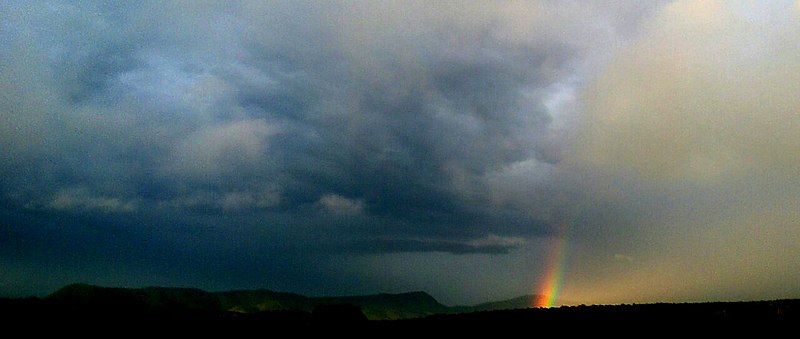 Foto de um arco-íris se abrindo entre nuvens escuras