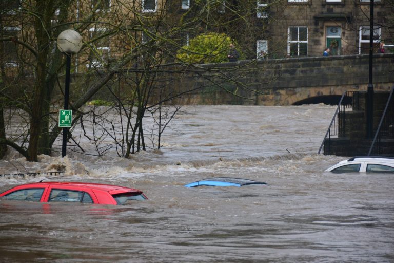 Foto de uma enchente levando carros rua abaixo.