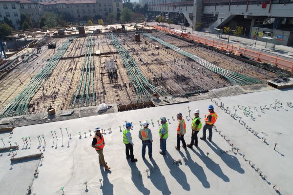 Foto aérea de vários engenheiros de pé em frente à construção de uma fundação.