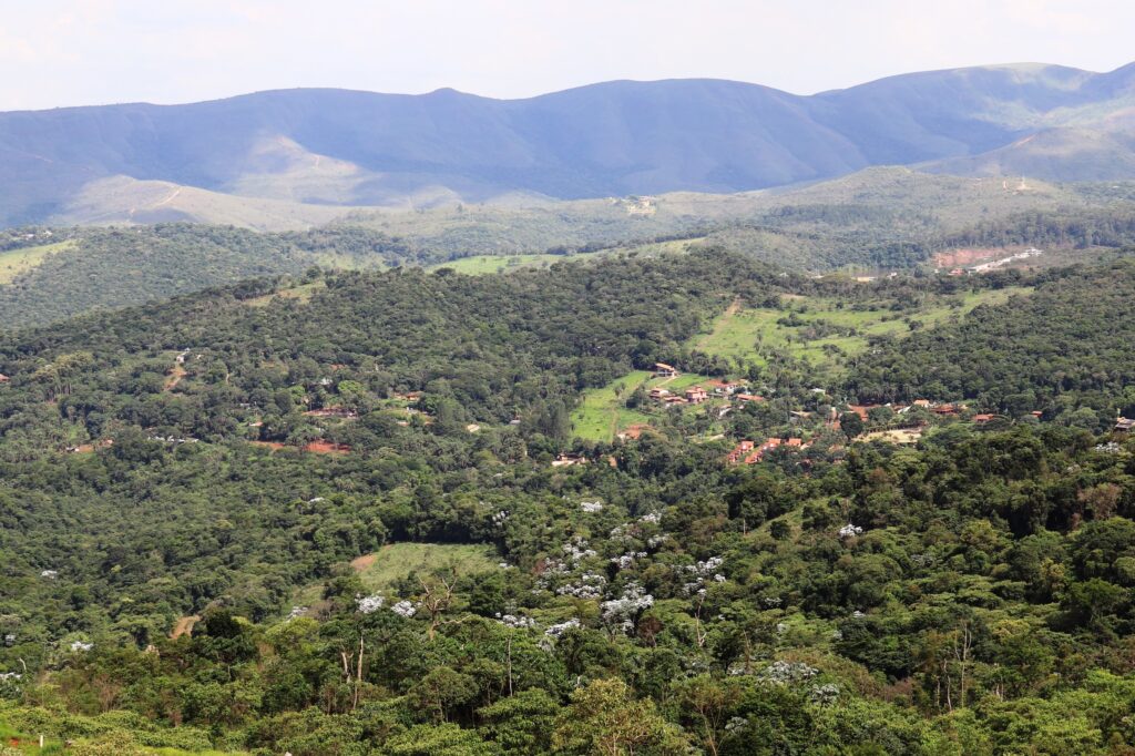 Foto aérea da zona a jusante de uma barragem de rejeitos em Minas Gerais, com diversas casas cercadas de vegetação. Montanhas ao fundo.