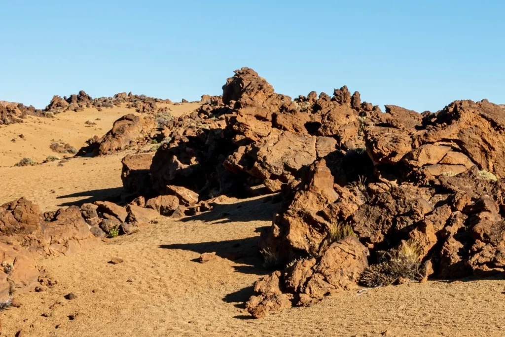 Rochas sedimentares avermelhadas em terreno arenoso, sob céu azul claro em área desértica