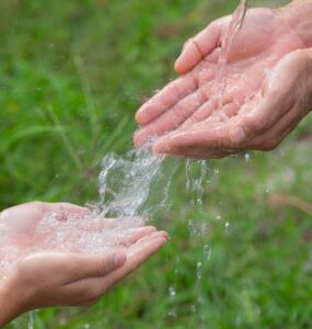 Mãos de um adulto passando água para as mãos de uma criança