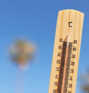Termômetro de madeira marcando temperatura próxima de 50°C sob céu azul claro, representando calor extremo.
