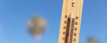 Termômetro de madeira marcando temperatura próxima de 50°C sob céu azul claro, representando calor extremo.