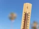 Termômetro de madeira marcando temperatura próxima de 50°C sob céu azul claro, representando calor extremo.