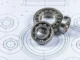 Rolamentos de esferas metálicos posicionados sobre desenho técnico de engenharia mecânica com vista detalhada em planta.
