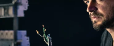 Eletricista com capacete de proteção analisando fios elétricos expostos durante manutenção