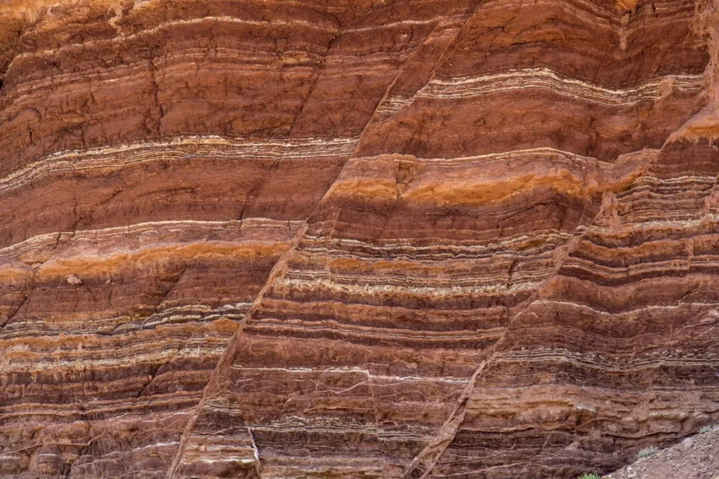 Estratigrafia de rochas sedimentares em tons avermelhados e ocres, mostrando camadas geológicas formadas ao longo de milhões de anos