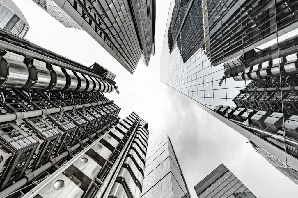 Perspectiva de arranha-céus modernos vistos de baixo, com fachadas de vidro e estruturas metálicas