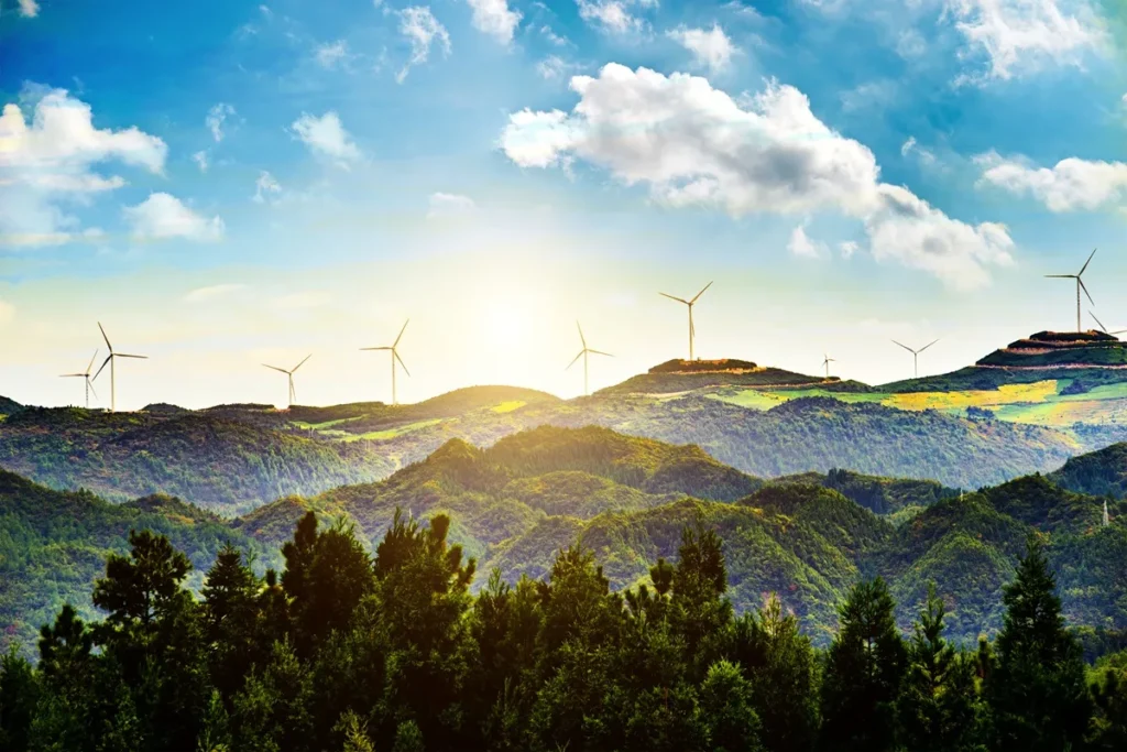 Turbinas eólicas em funcionamento sobre montanhas verdes ao pôr do sol, simbolizando energia renovável e sustentabilidade.
